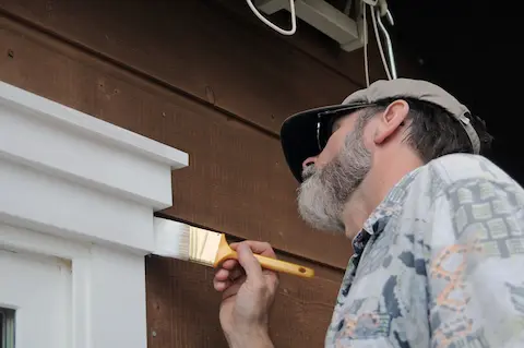 A professional house painter from Oregon City Painting carefully painting exterior trim on a house.